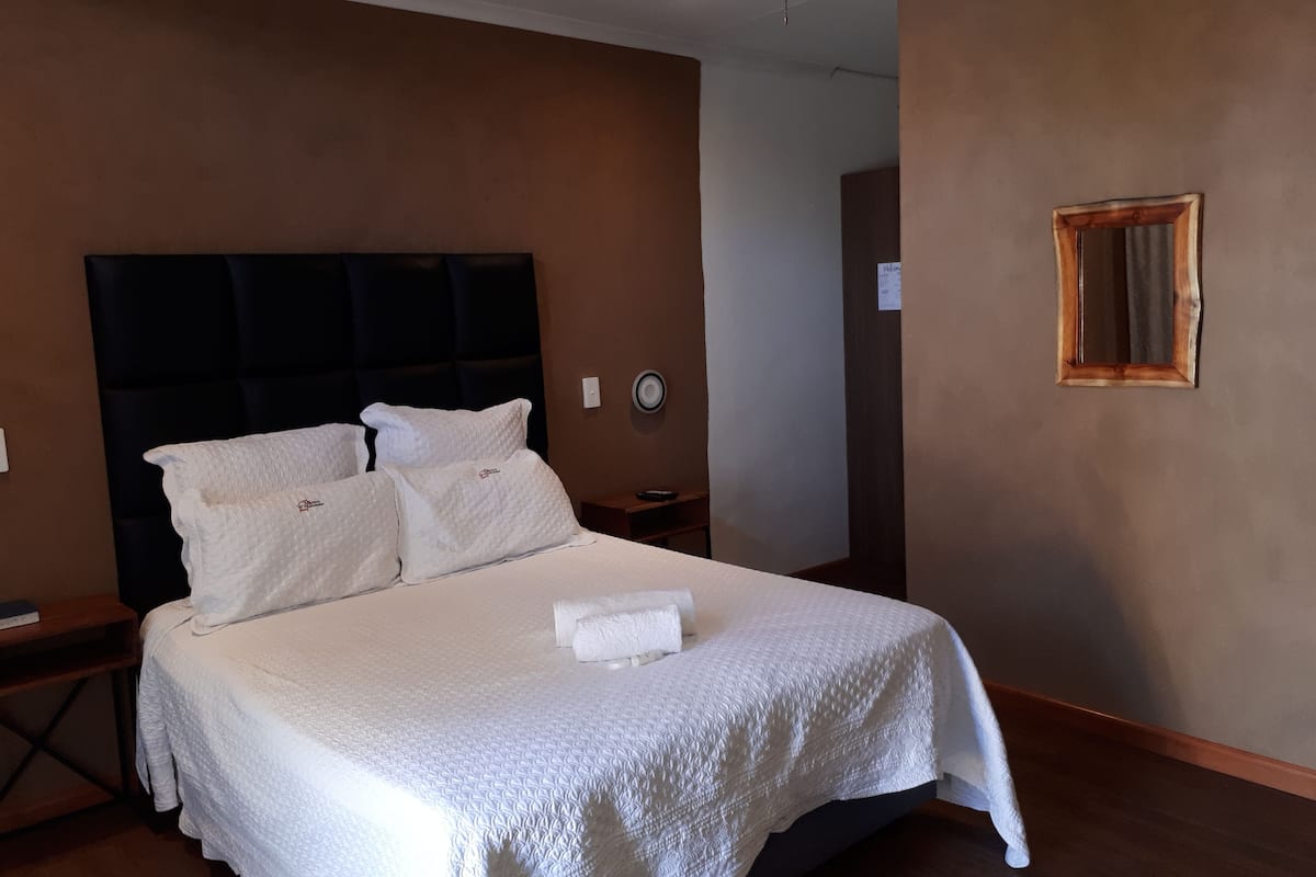 Een netjes opgemaakt bed met witte lakens, een donkere hoofdbord en een klein nachtkastje met een lamp.