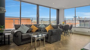 A modern living room with a large sofa, a glass coffee table, and a dining area with chairs and a table. - Penthouse With City Skyline Views - Balcony  - King Bed - Netflix (birmingham)