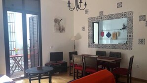 Een woonkamer met een eethoek, een kroonluchter, een grote spiegel en uitzicht door een glazen deur.