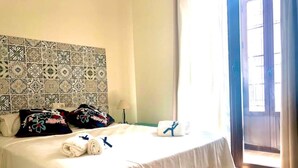 Een hotelkamer met een bed, een hoofdbord met een patroon, een raam met gordijnen en een nachtkastje met een lamp.
