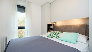 A modern bedroom with a large bed, a headboard with integrated lighting, and a view of greenery outside. - Hedera A12 (Dubrovnik)