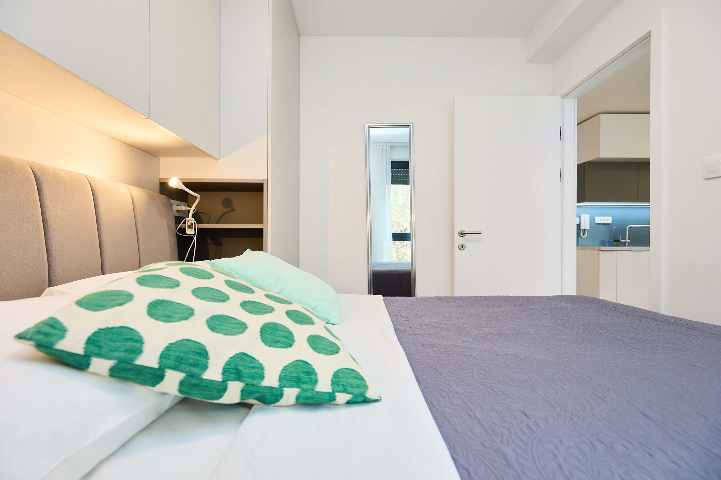 A bedroom with a bed, a nightstand, a mirror, and a door leading to a bathroom.