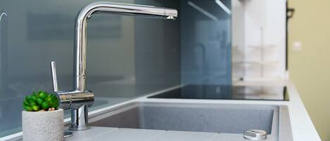 A modern kitchen sink with a chrome faucet, a small potted plant, and a white countertop.
