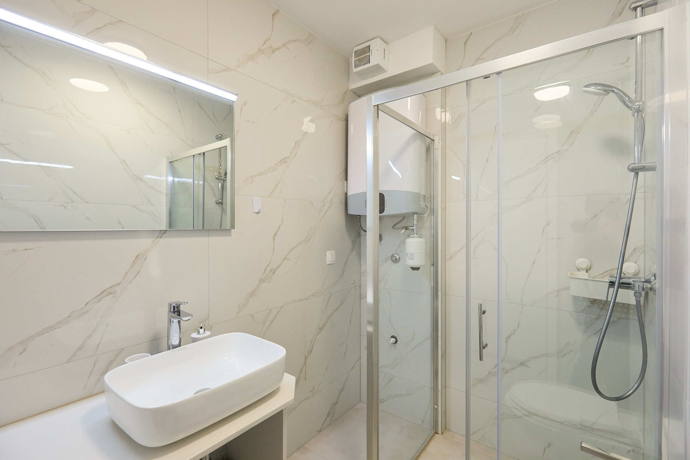 A modern bathroom with a marble sink, a glass-enclosed shower, and a built-in mirror.