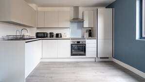 A modern kitchen with white cabinets, a built-in oven, and a stainless steel range hood. - Stunning 1-bed Apartment in Hemel Hempstead (Hemel Hempstead)