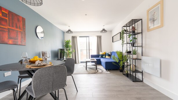 A modern living room with a dining area, a blue sofa, a black bookshelf, and a large abstract painting on the wall. - Stunning 1-bed Apartment in Hemel Hempstead (Hemel Hempstead)