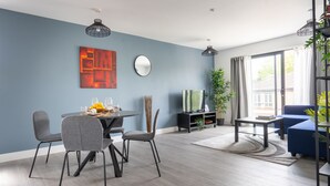A modern living room with a dining area, featuring a blue wall, grey furniture, and a large window with curtains. - Stunning 1-bed Apartment in Hemel Hempstead (Hemel Hempstead)