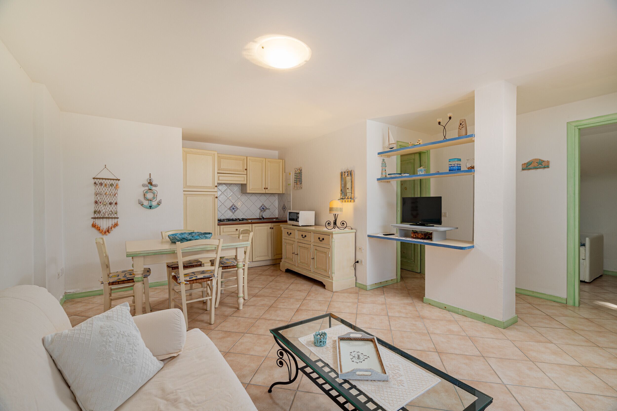 Un espacio habitable compacto con comedor, kitchenette y un televisor sobre una estantería.