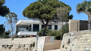Et moderne hus med et stort træ foran, en stenvæg og en klippefyldt forgrund.