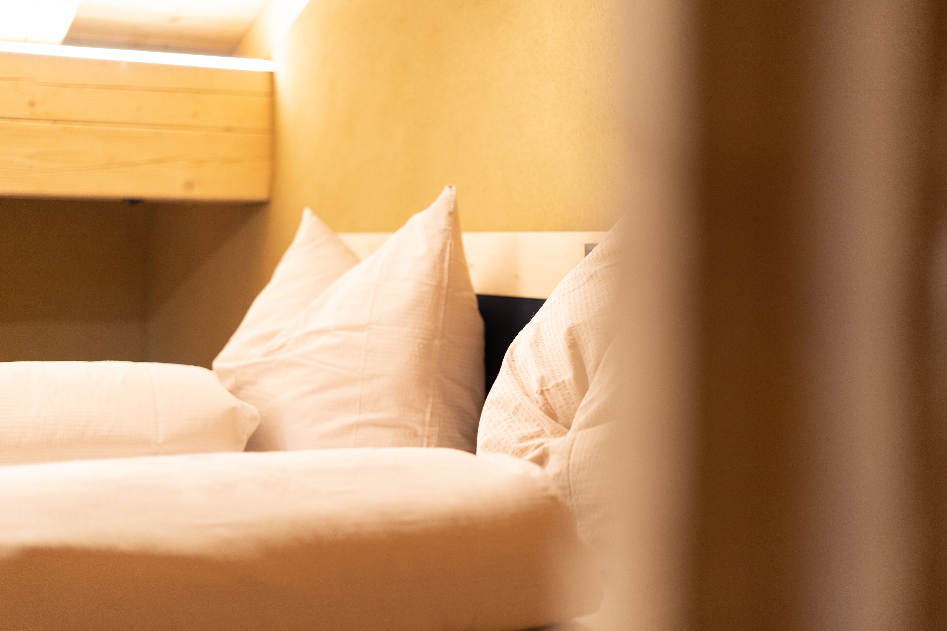 A bed with white bedding and pillows, a wooden headboard, and a wooden shelf above the bed.