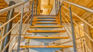 Una escalera en espiral de madera con barandillas de metal y pasamanos de cuerda, que sube a un piso superior.