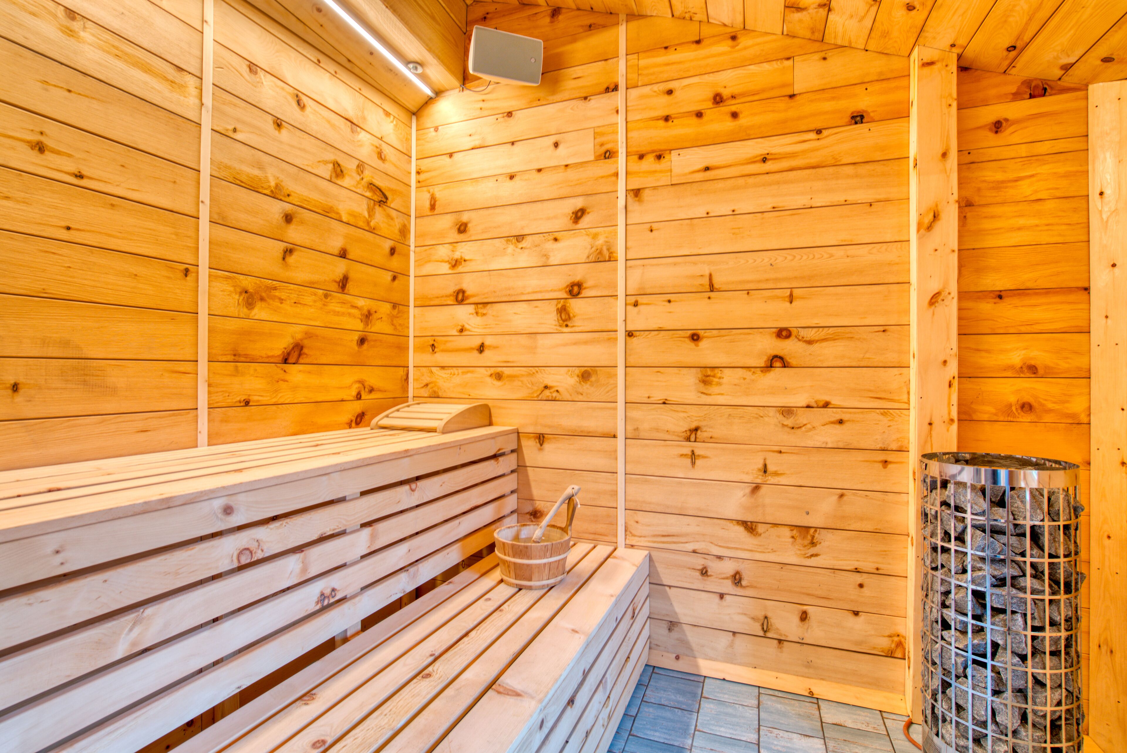 Una sauna con bancos de madera, un calentador de piedra y un recipiente metálico.