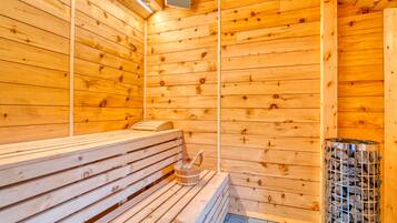 Una sauna con bancos de madera, un calentador de piedra y un recipiente metálico.