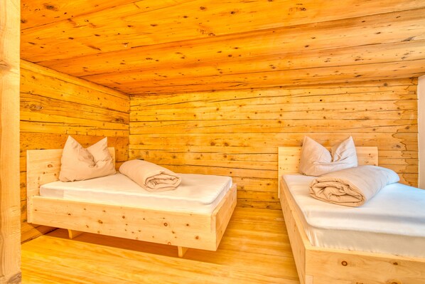 Habitación de cabaña de madera con dos camas de madera, cada una con almohadas y una colcha doblada.