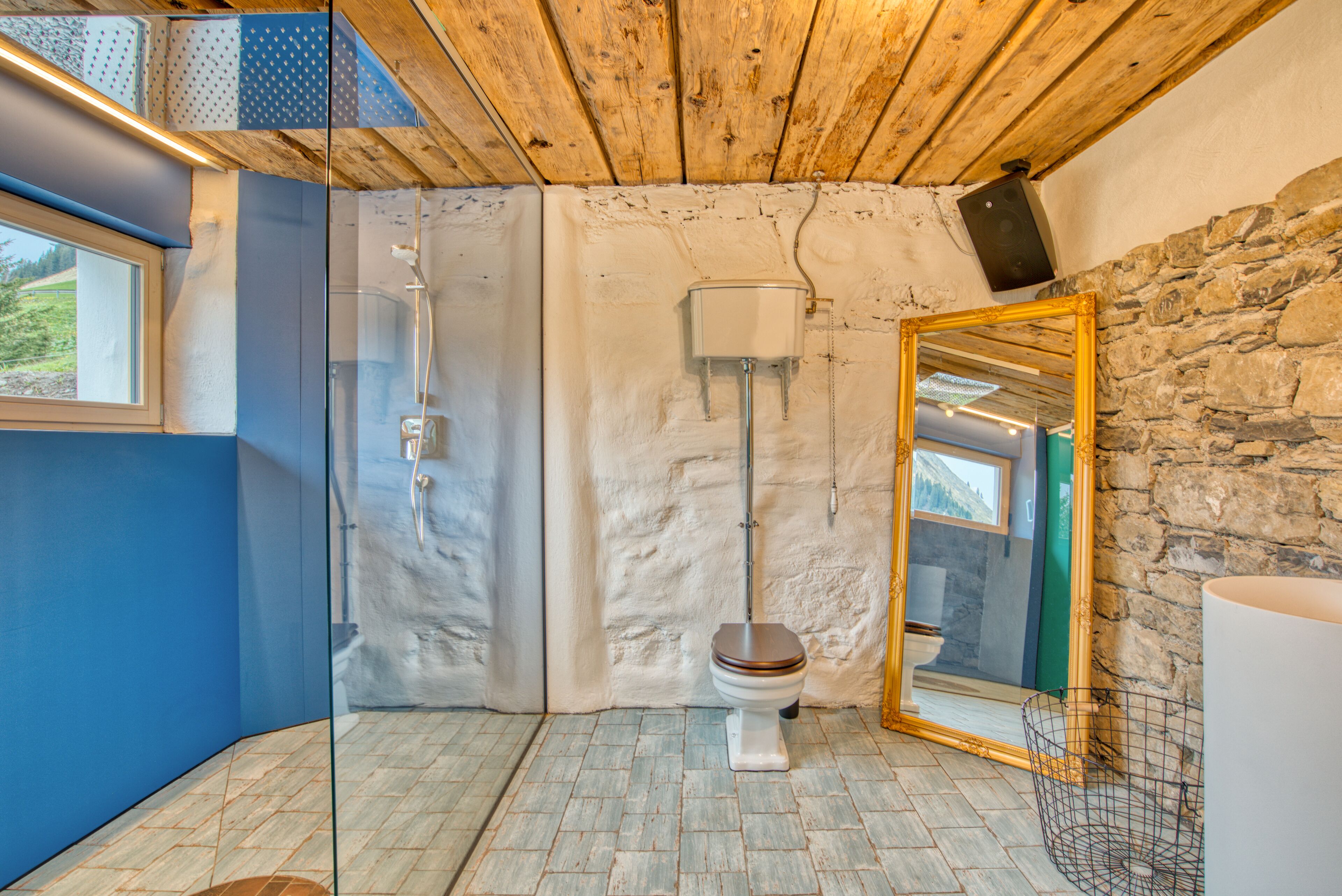 Un baño con techo de madera, pared de piedra, cabina de ducha de vidrio y un espejo grande.