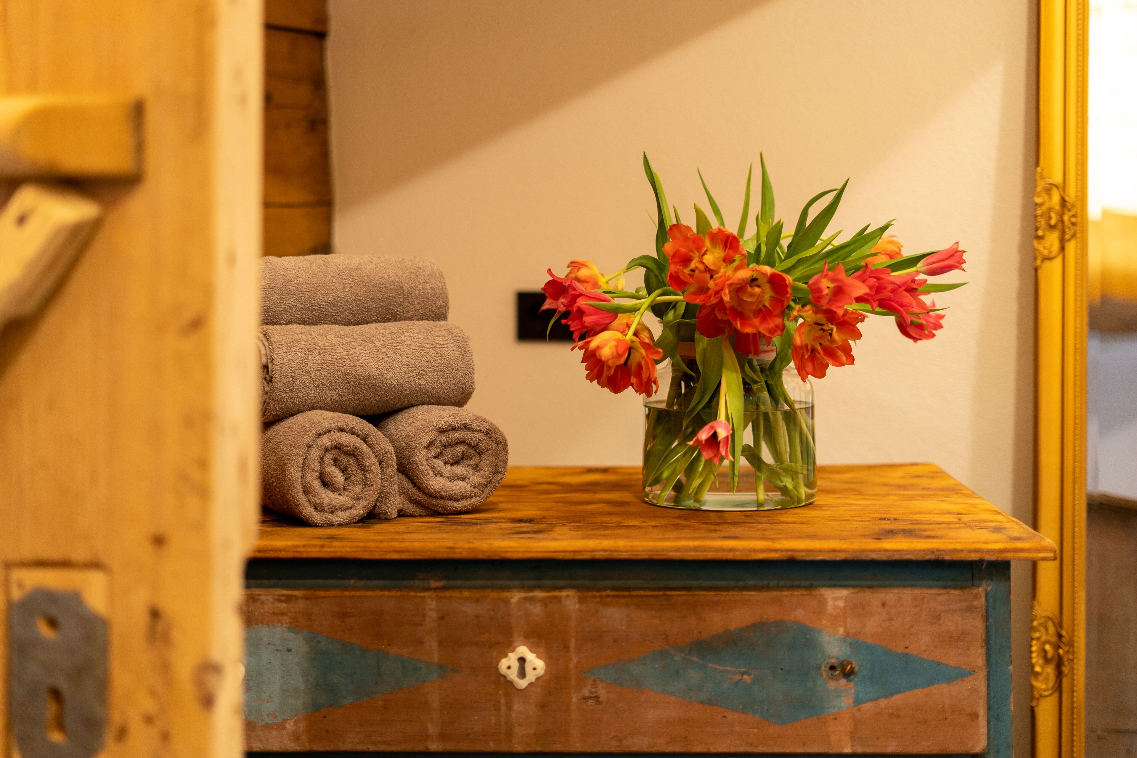 A wooden dresser with rolled towels and a vase of flowers.