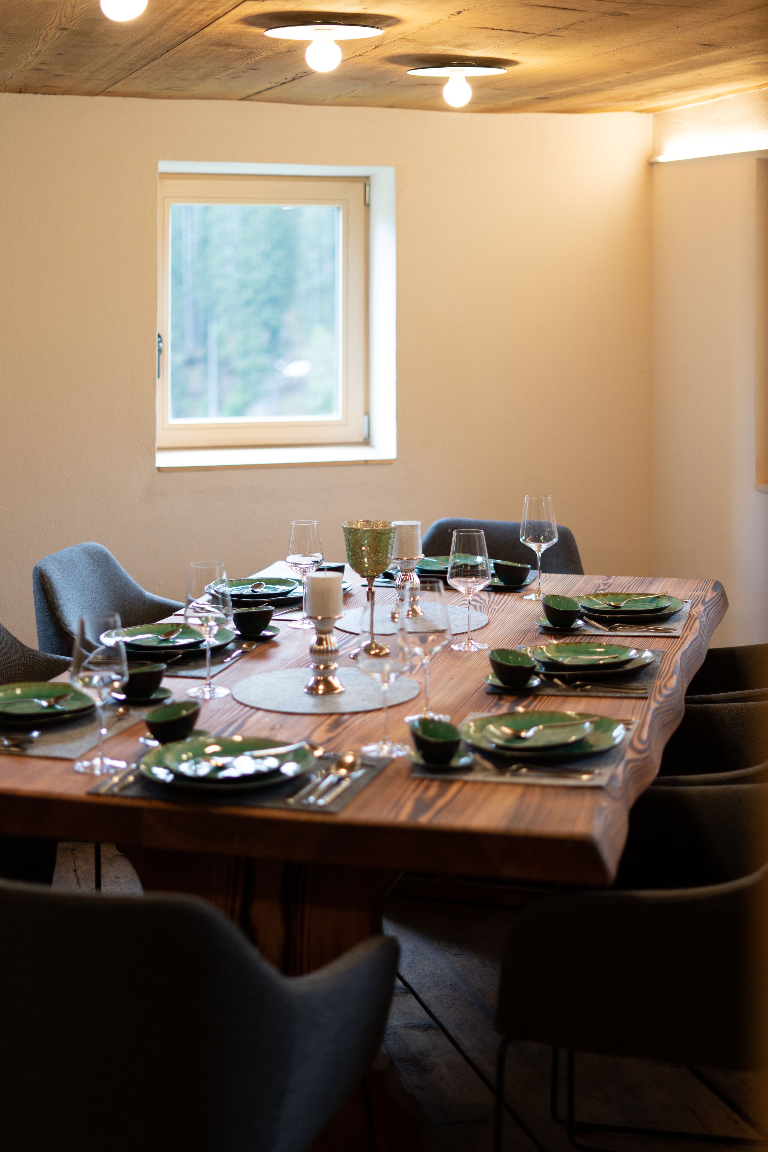 A dining table set with green plates, wine glasses, and cutlery, with a window above.