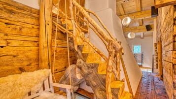 A rustic wooden interior with a wooden staircase, a fur-covered bench, and a large tree trunk.