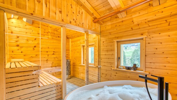 Una cabaña de madera con un jacuzzi grande, pisos de madera y un ventanal con vistas al verdor.