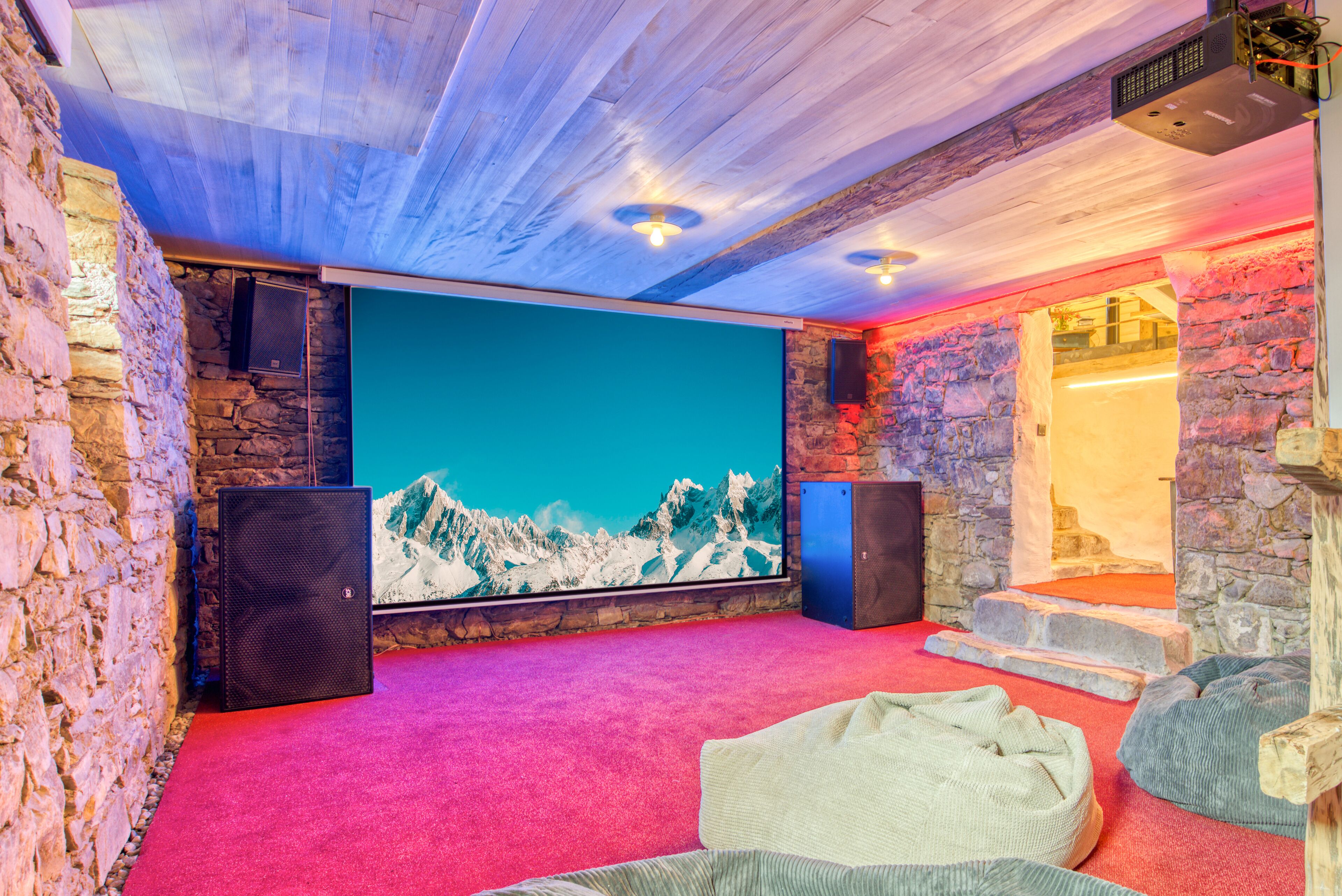 Ein gemütlicher Raum mit einer Steinwand, einem großen Bildschirm und einem roten Teppich.