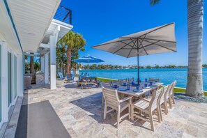 Un patio al aire libre con mesa y sillas, un paraguas grande y vista al agua.