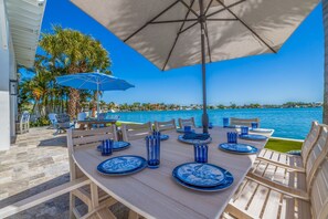 Un área de comedor al aire libre con una mesa dispuesta para seis personas, platos azules y vasos, todo bajo un paraguas grande.
