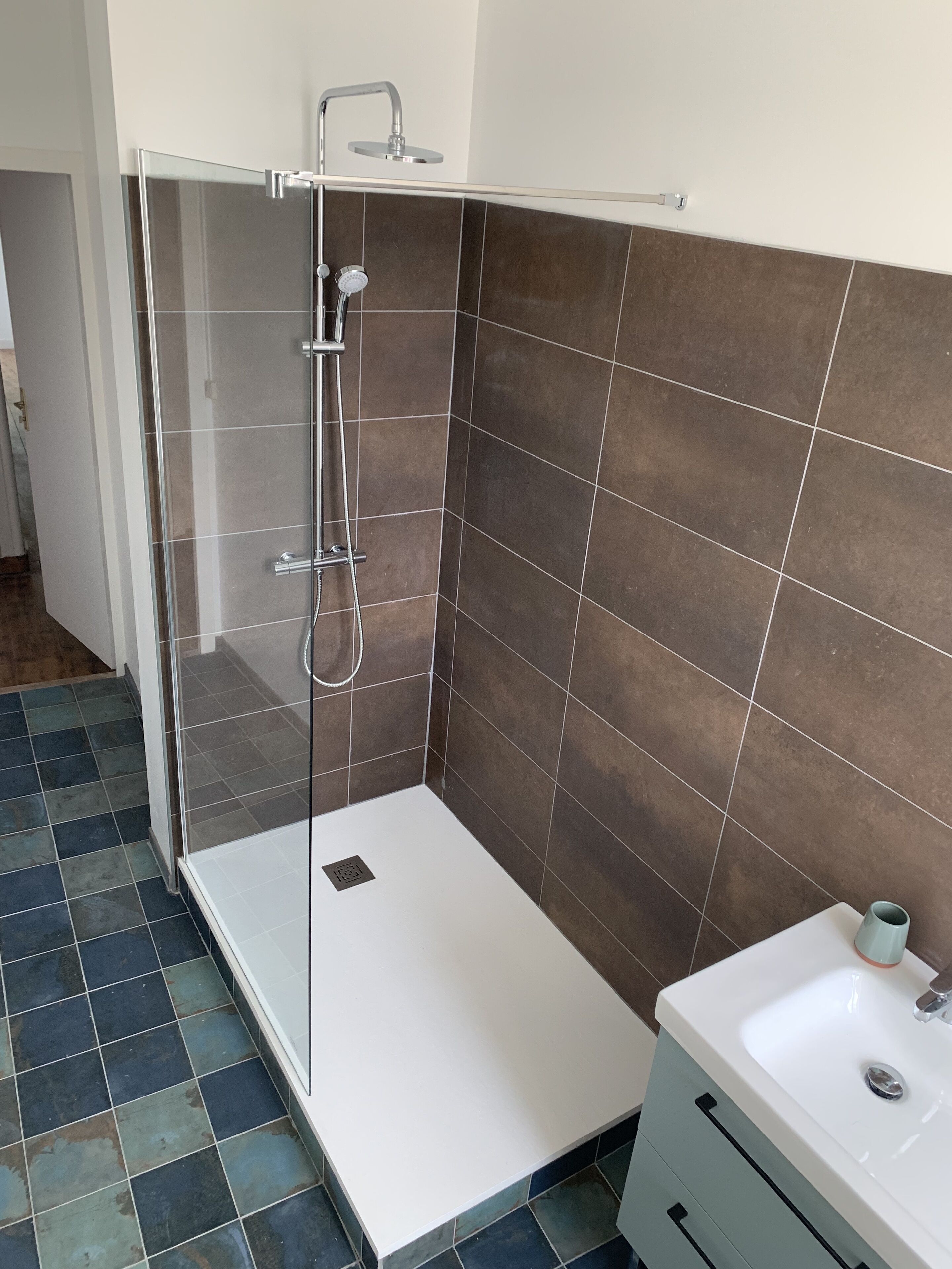 A modern bathroom with a glass-enclosed shower, a white sink, and a tiled floor.