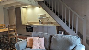 A modern living room with a grey sofa, a wooden dining table, and a kitchen area with a built-in oven and sink. - Charming self-catered two story, sleeping four with gated garden and shared pool (Soyaux)