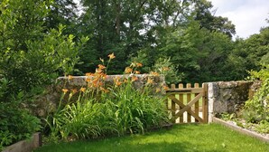 A stone wall with a wooden gate, surrounded by lush greenery and flowering plants. - Charming self-catered two story, sleeping four with gated garden and shared pool (Soyaux)