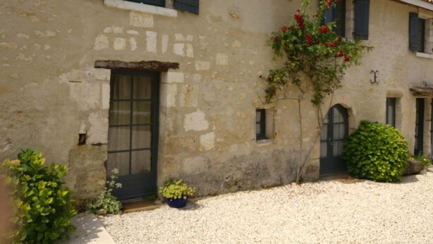 A rustic building with a stone facade, a wooden door, and a small garden area with gravel and potted plants. - Charming self-catered two story, sleeping four with gated garden and shared pool (Soyaux)