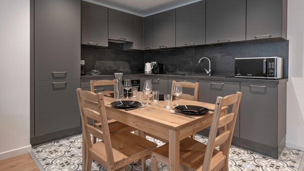 Una cocina moderna con armarios grises, una mesa de comedor de madera con platos y vasos, y un microondas en la encimera.
