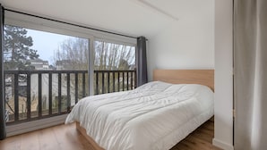Un dormitorio con un ventanal grande, una cama con ropa de cama blanca y un cabecero de madera.