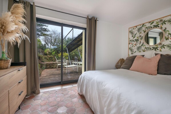 A bedroom with a large bed, a sliding glass door leading to an outdoor patio, a wooden dresser, and a wall-mounted mirror.