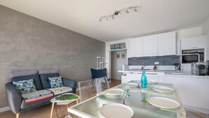 A modern kitchen with white cabinets, a microwave, and a dining area with a glass table and chairs. - Seafront apartment balcony in La Baule - 6 guests (La Baule-Escoublac)