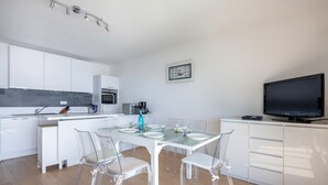 A modern kitchen with white cabinets, a dining table with clear chairs, and a flat-screen TV. - Seafront apartment balcony in La Baule - 6 guests (La Baule-Escoublac)