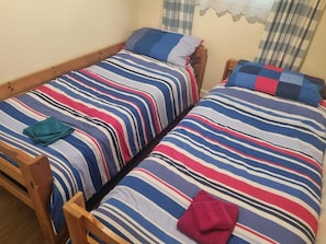 A room with two wooden beds, each with striped bedding and pillows.