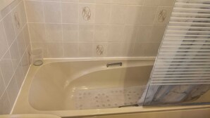 Un bagno con una vasca, pareti piastrellate di bianco e una finestra.