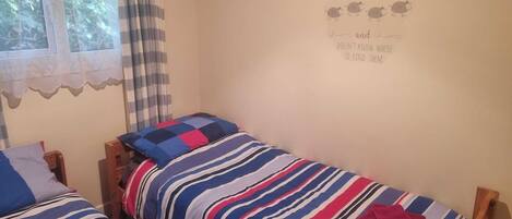 A bedroom with two single beds, a window with curtains, and a wall with a children's rhyme.