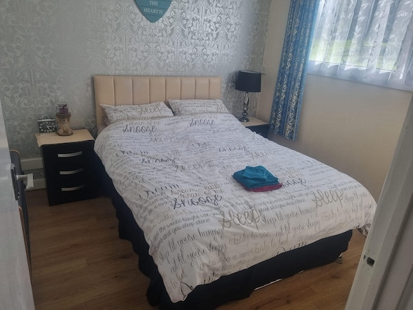 A bedroom with a bed, a nightstand, a lamp, and a wall clock.
