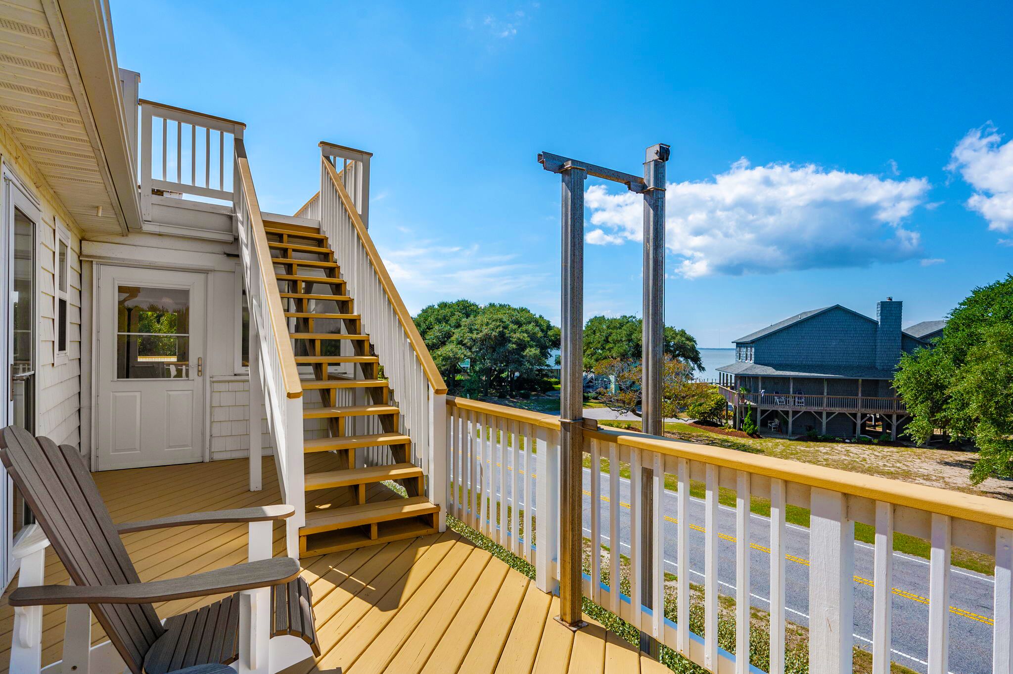 A wooden deck with a staircase leading to a white door, a white picket fence, and a view of a building across a road.