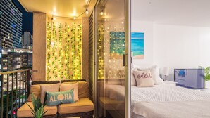 A modern hotel room with a balcony, a glass wall with greenery, and a bed with a view of the city. - Renovated Waikiki Studio! City View, Full Kitchen, Free Wi-Fi & Parking, Pool (Honolulu)