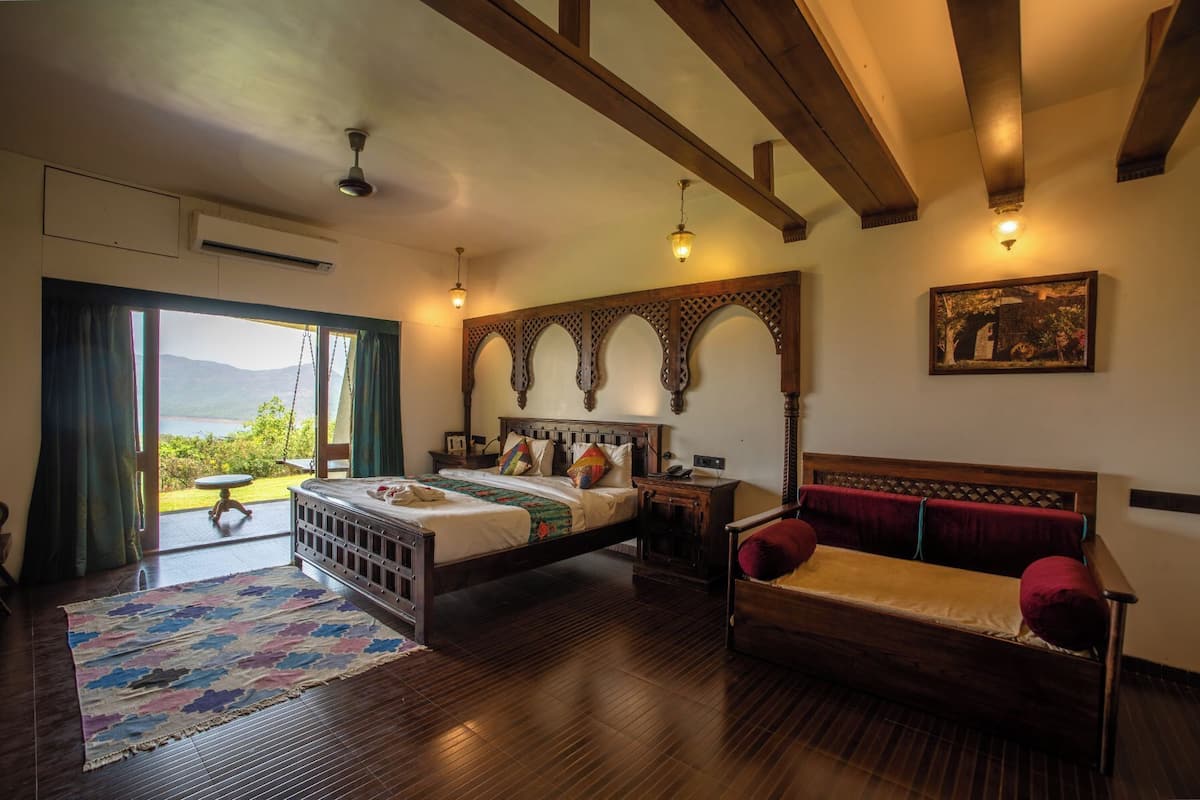 A bedroom with a large bed, a wooden bench, a view of the outdoors, and a ceiling fan.