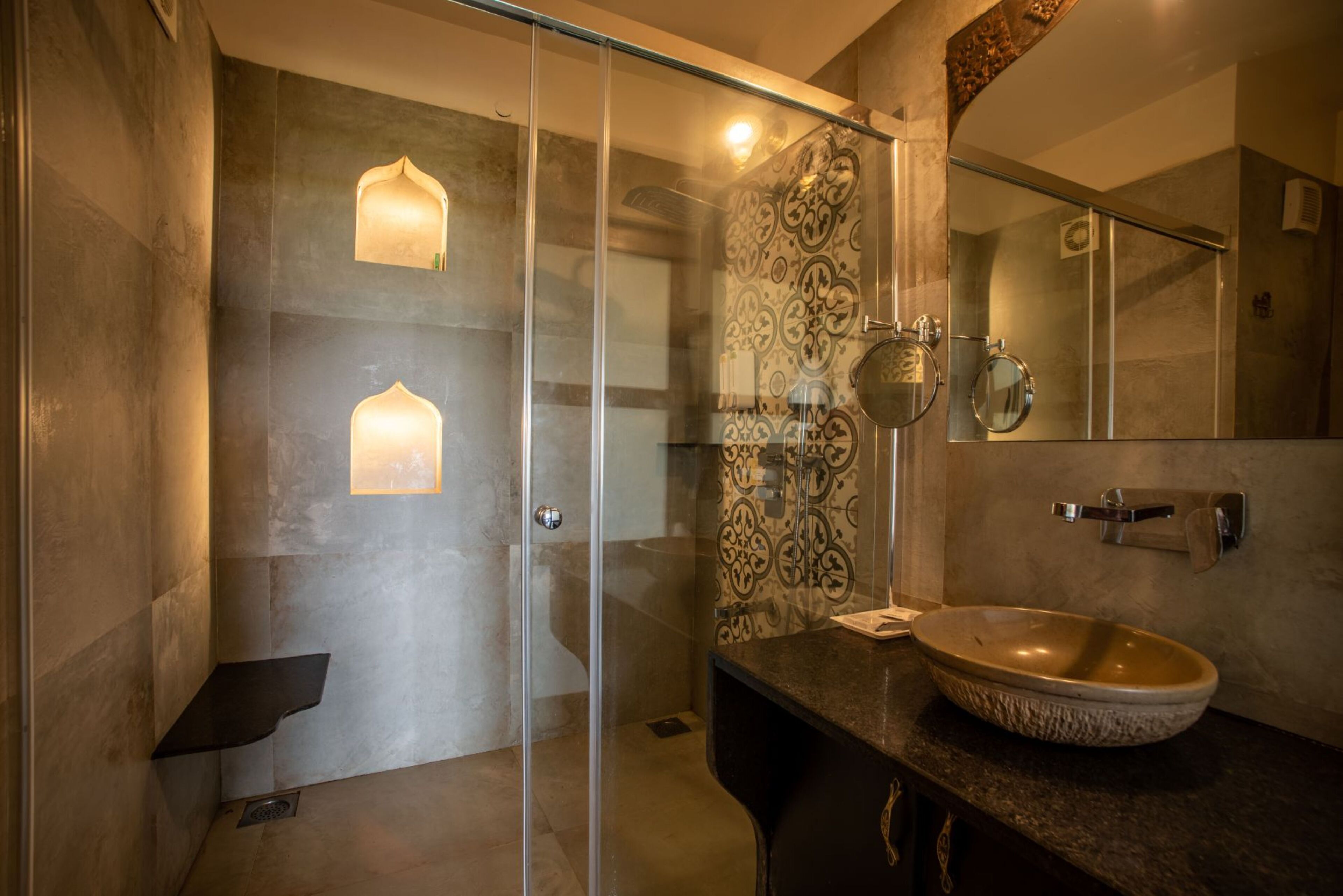 Un baño moderno con ducha envuelta en vidrio, un espejo grande y un lavamanos de piedra.