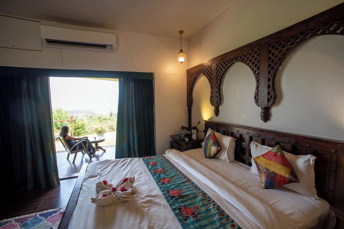 A hotel room with a bed, a view through a window, and a balcony.