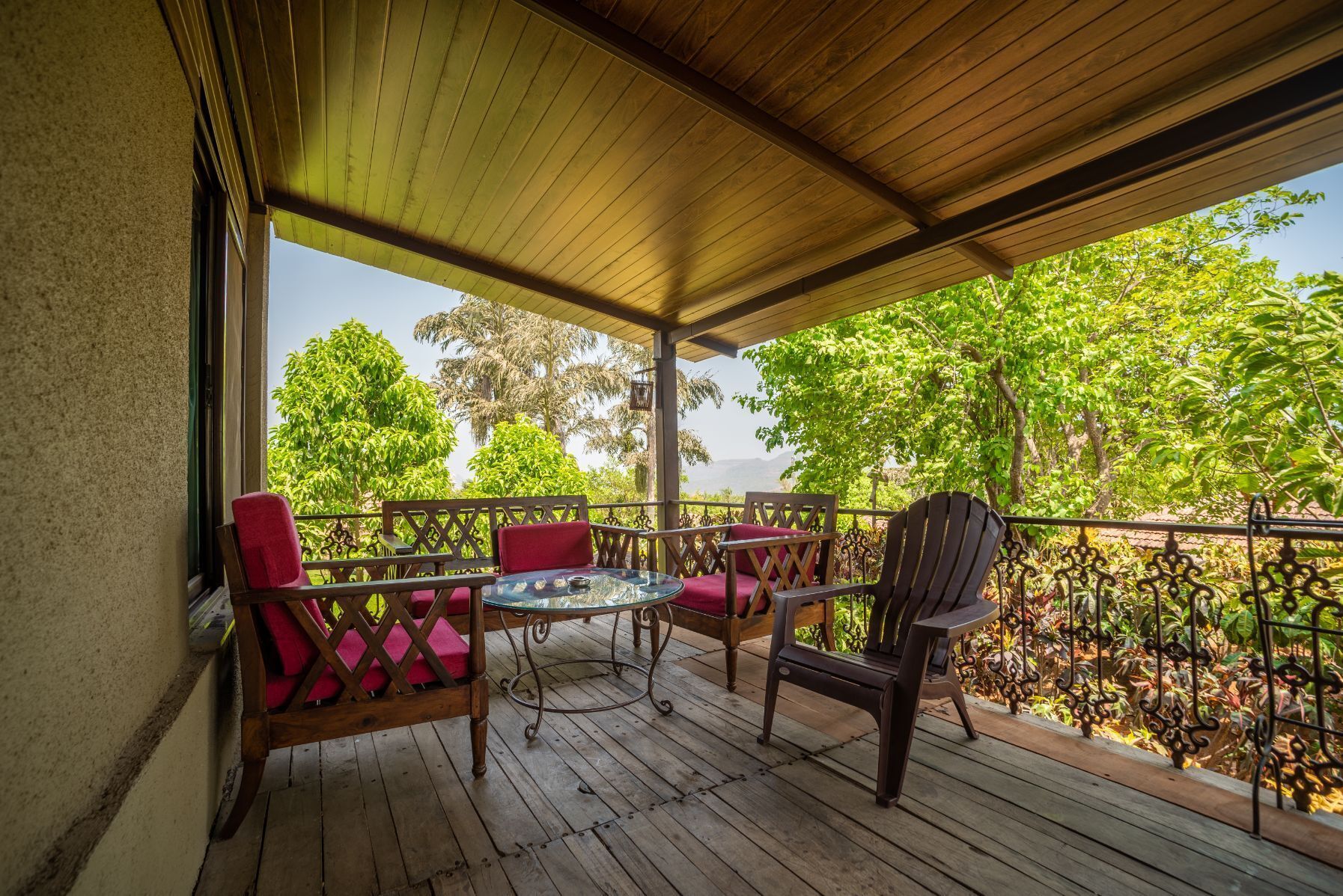 A covered outdoor seating area with wooden furniture and a view of lush greenery.