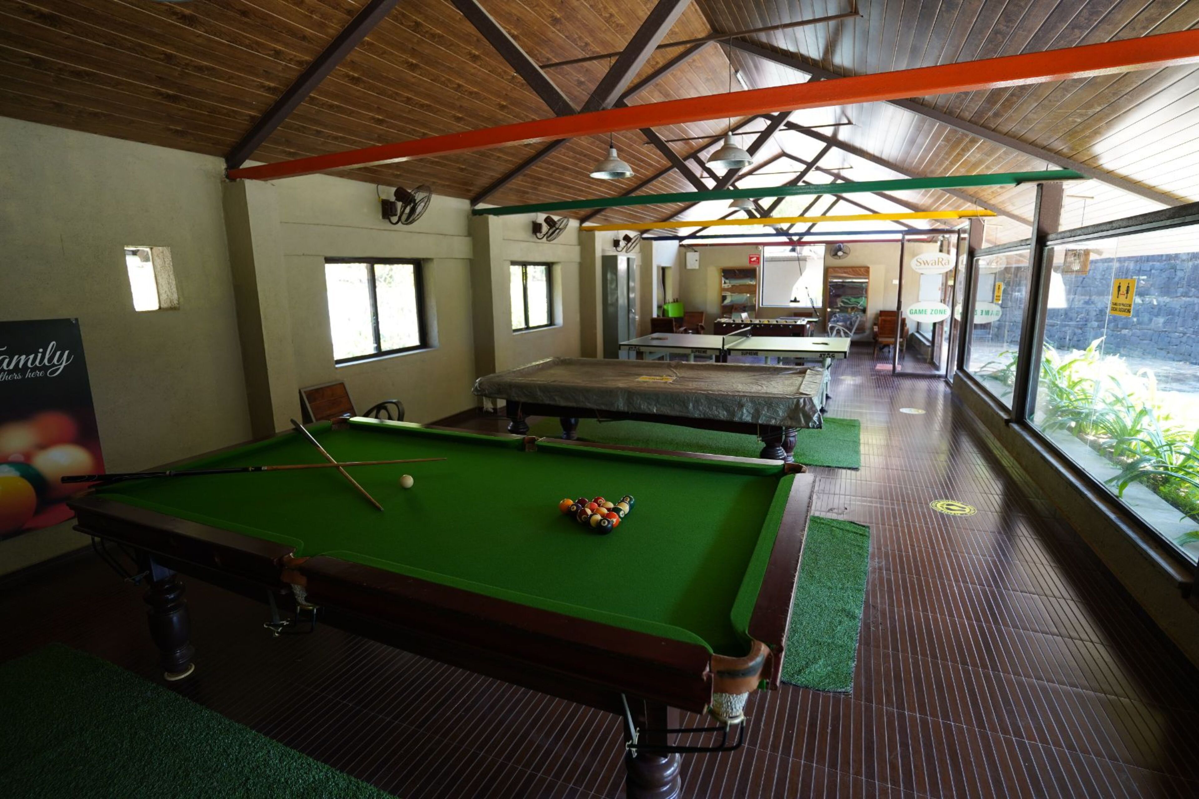 Une table de billard avec une queue, un porte-billes et un tapis vert. La pièce contient plusieurs tables et chaises disposées de manière harmonieuse.