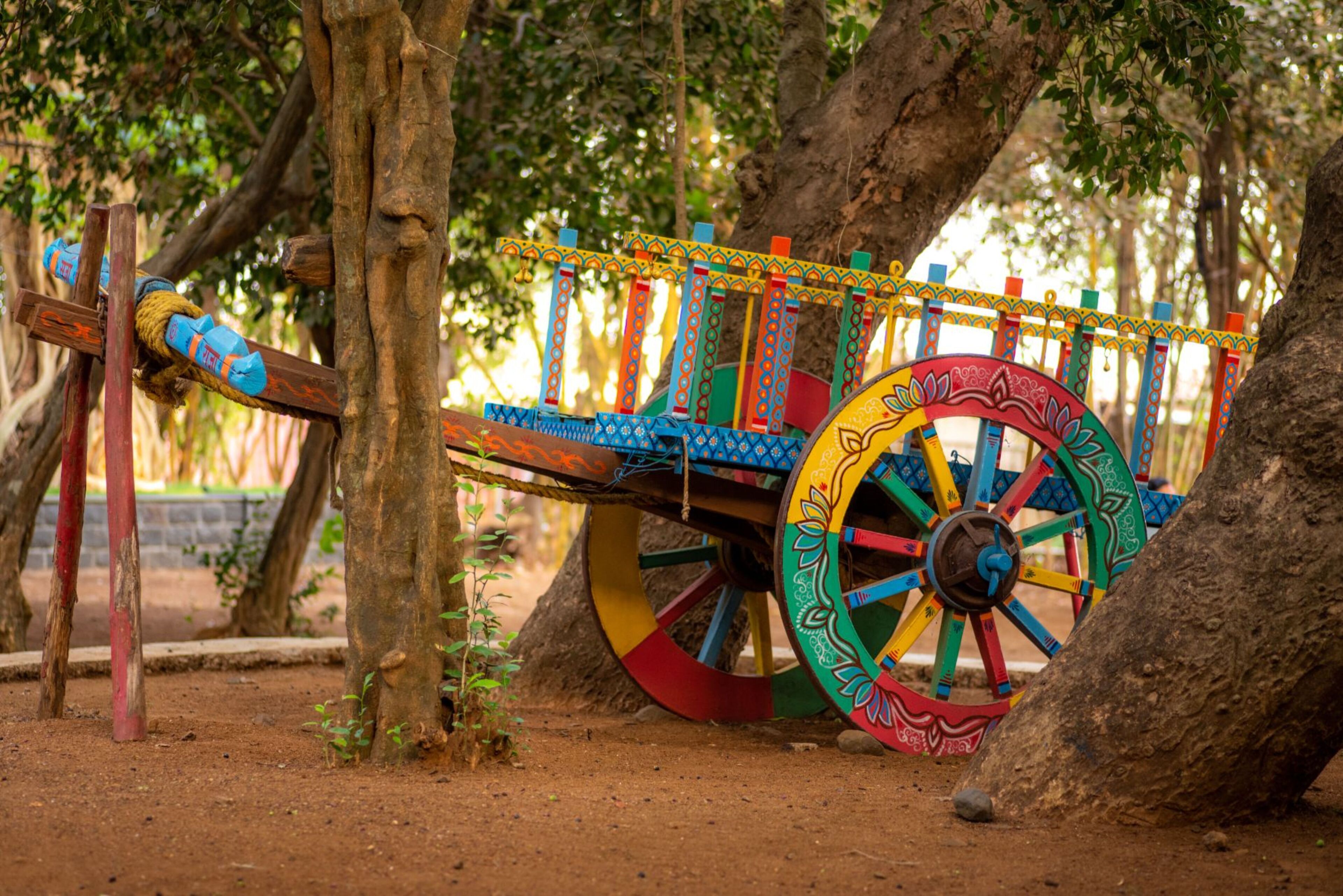 A colorful wooden structure with a wheel and rope mechanism, surrounded by trees.