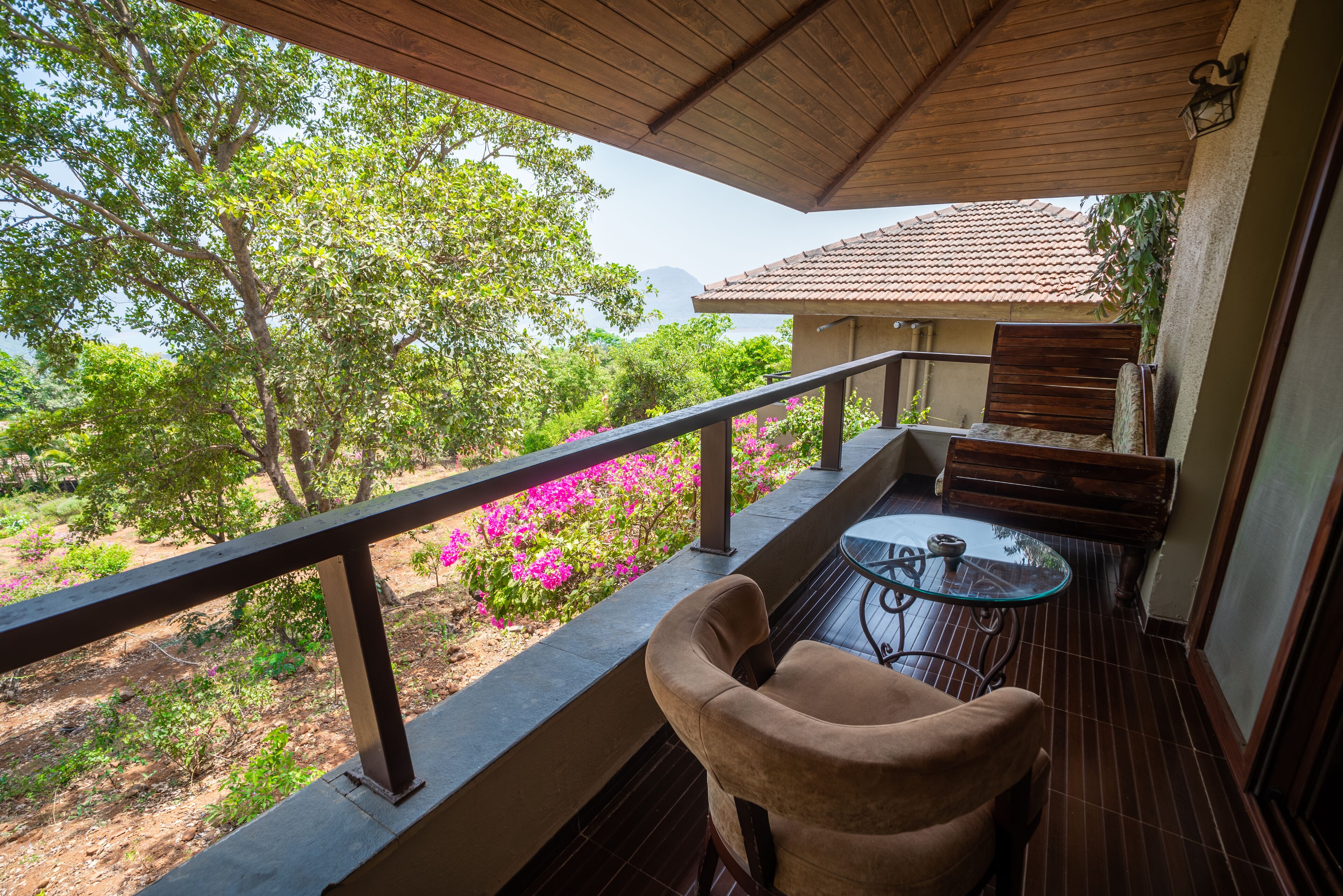 A balcony with a wooden railing, a glass table, and a cushioned chair.