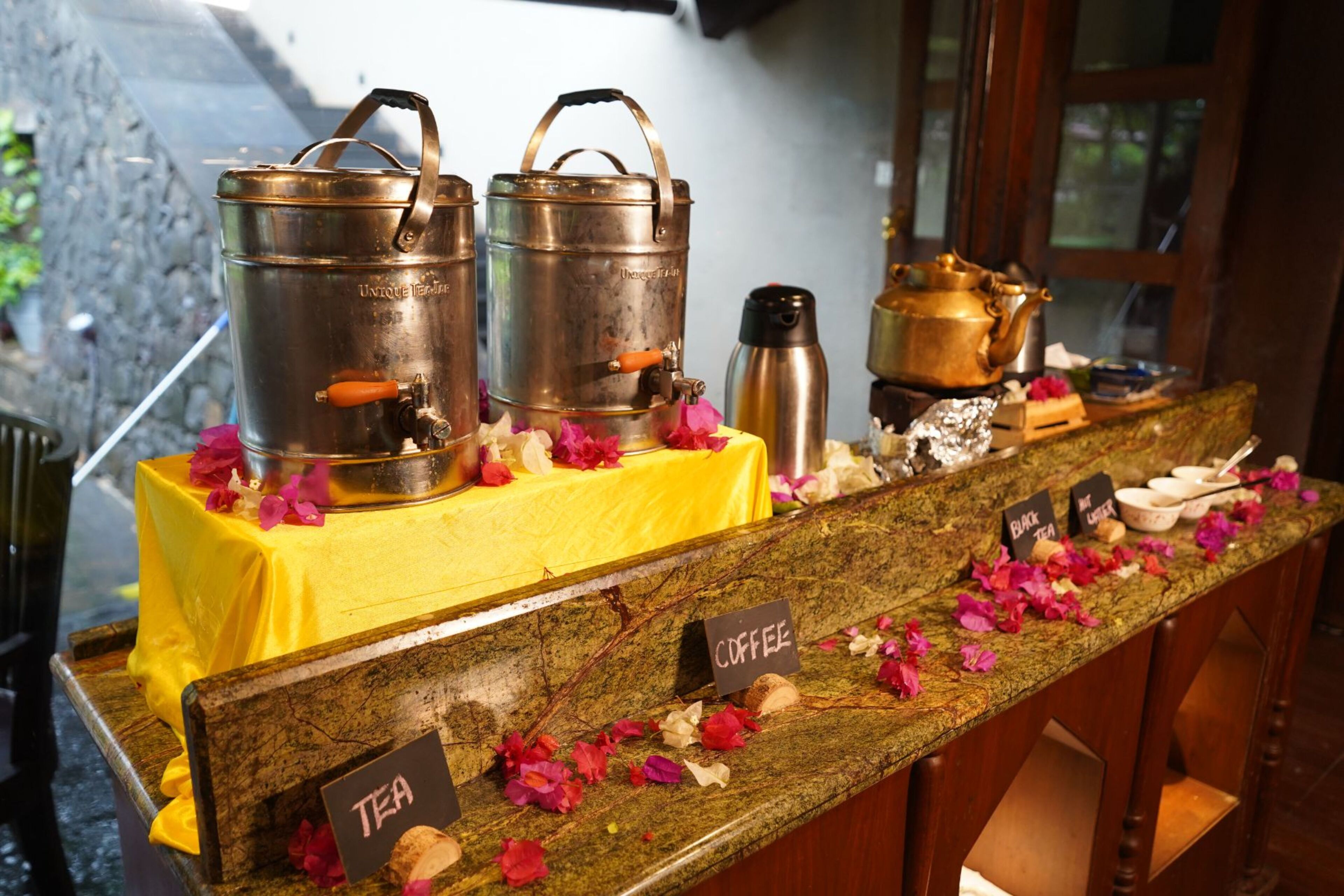 A coffee and tea station with metal containers and a yellow tablecloth.
