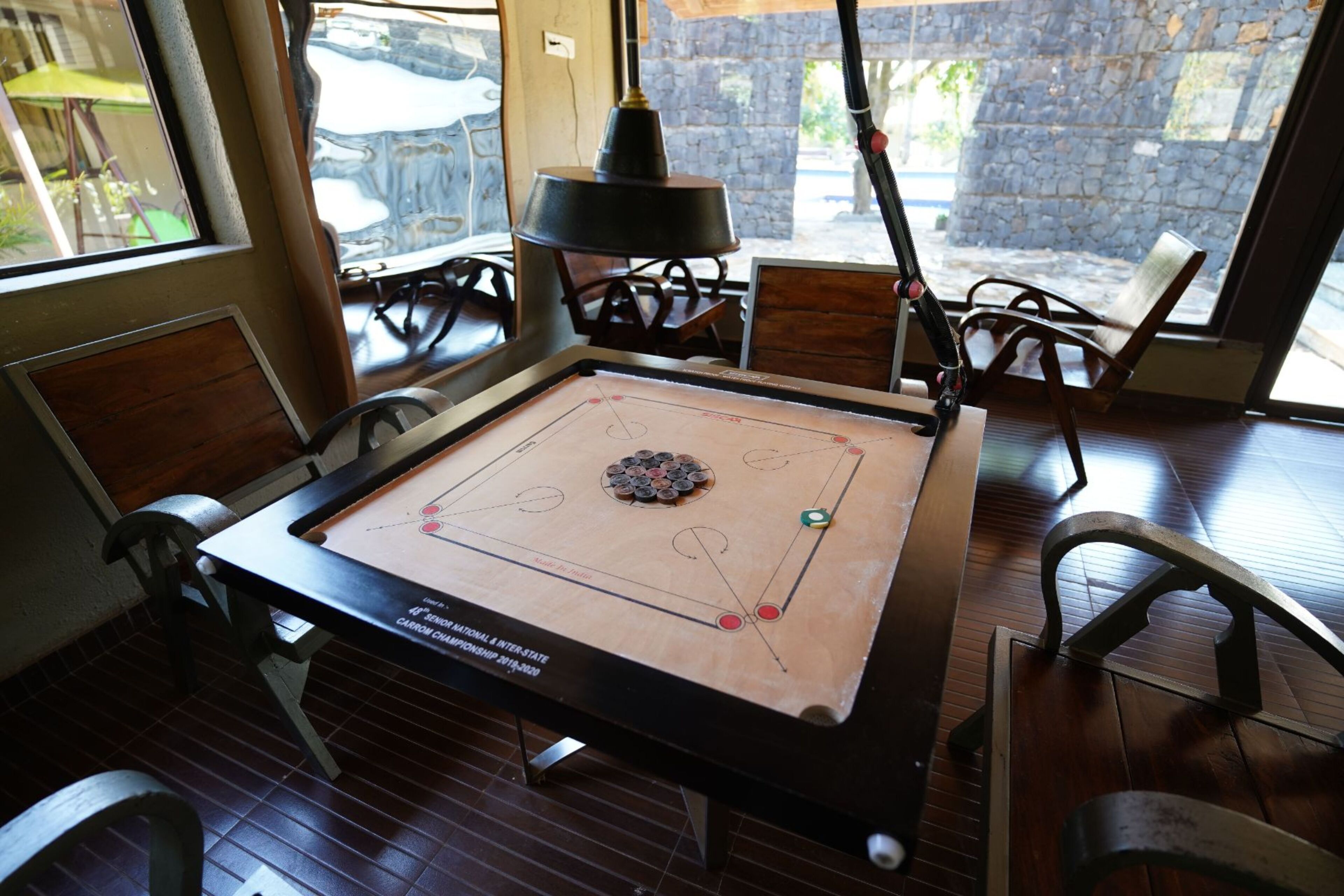 Una mesa de shuffleboard con superficie de madera y barandillas metálicas, ubicada en una habitación con suelo de madera y paredes de piedra.
